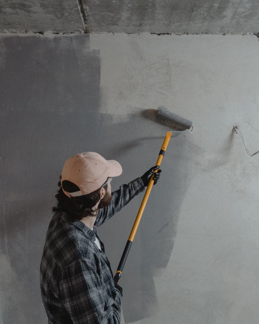 A painter rolling fresh paint across a bare interior wall
