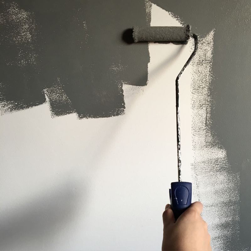 A roller laying an even coat of grey paint over a white wall