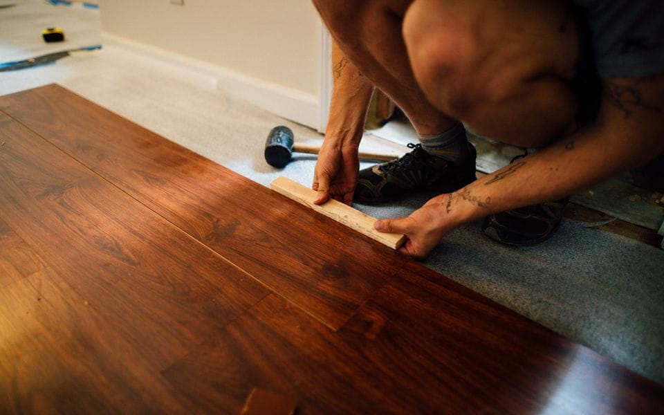 Plank flooring being tapped into place across a subfloor