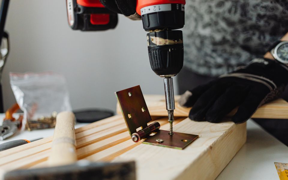 A cordless drill driving a screw through a hinge into a length of timber