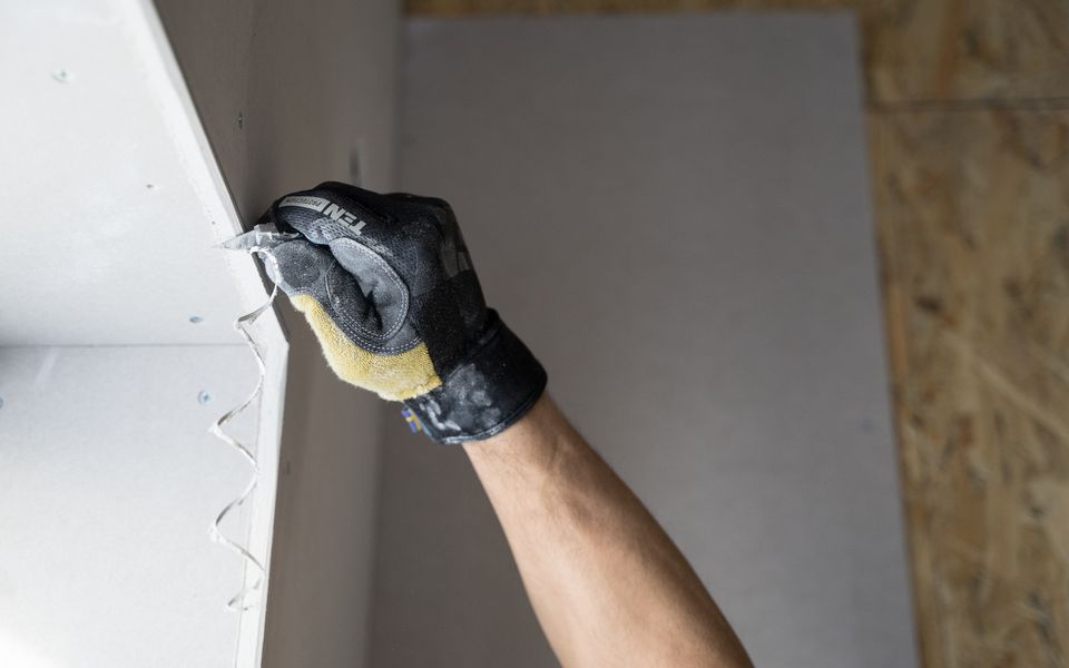 A gloved hand drawing joint compound along a drywall seam