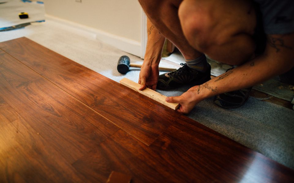 Plank flooring being tapped into place across a subfloor