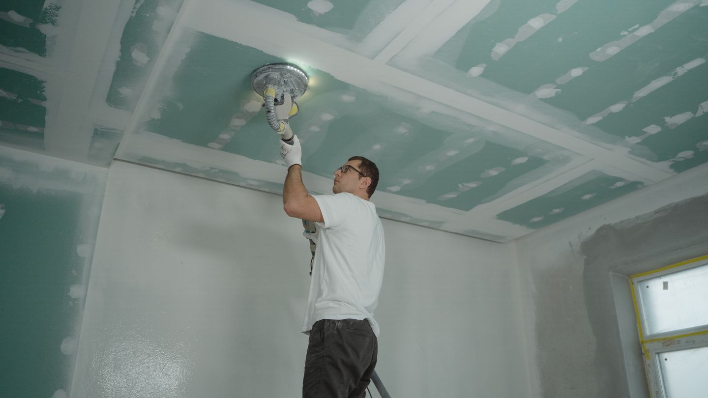 A worker sanding a ceiling smooth during a repair