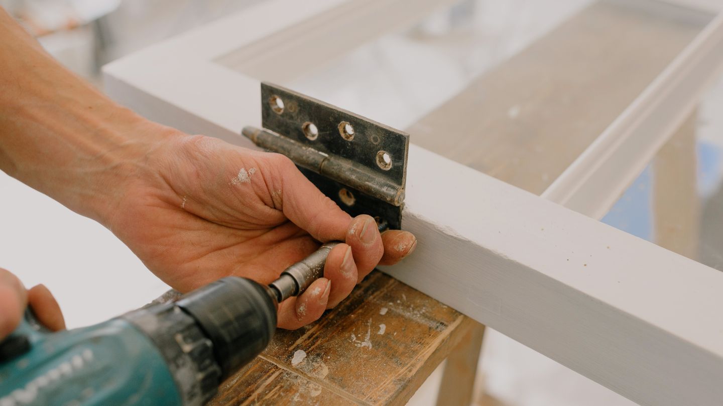 A hinge being screwed onto a freshly painted door frame