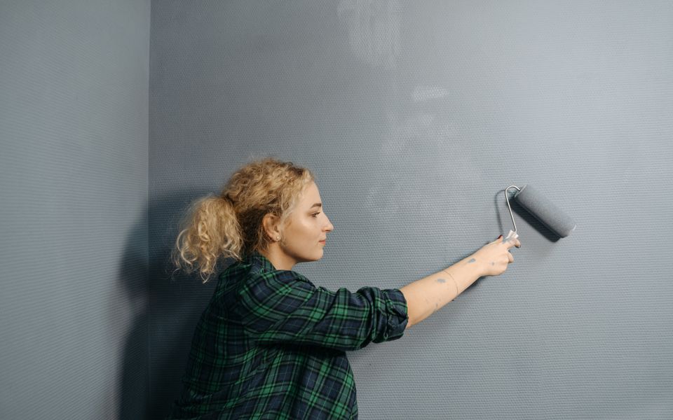A painter rolling grey paint across an interior wall